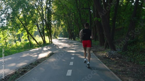 Wallpaper Mural Slow motion fit man wearing black shirt and red shorts running along bike lane in park on sunny morning. Following shot athlete doing cardio training outside. Concept of fitness Torontodigital.ca