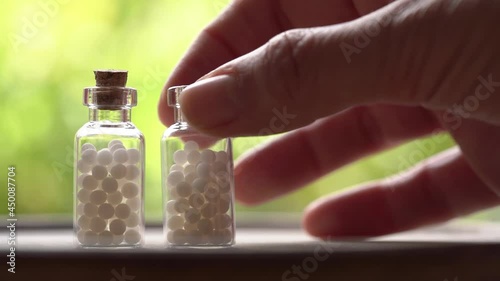 Two bottles of homeopathic remedies standing on a table, a hand taking one of them. Slow motion.