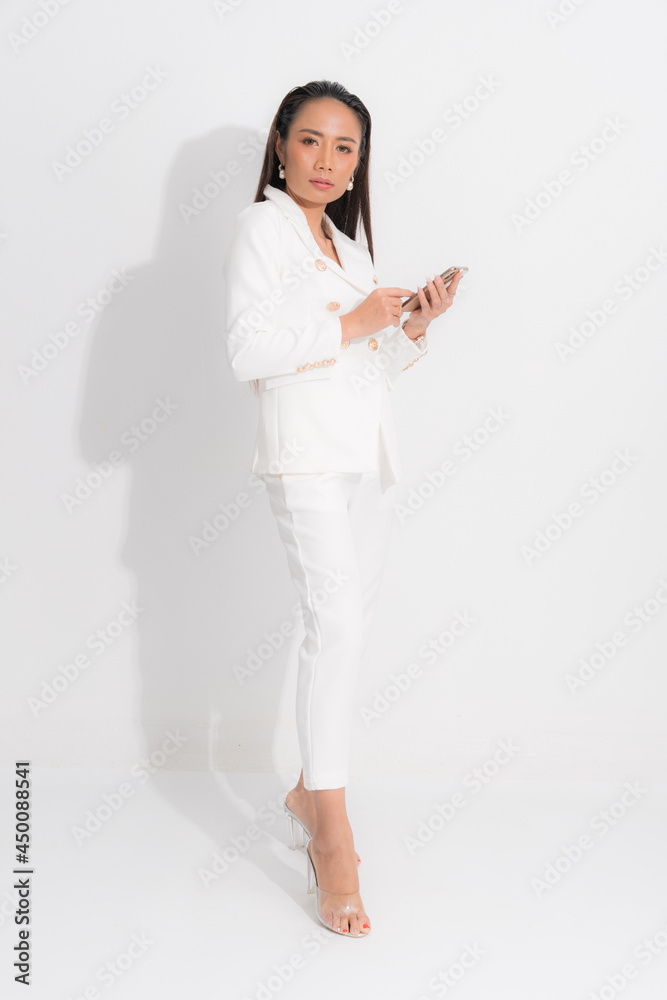 Fashion style catalog clothing for business woman black long hair natural make up wear white suit costume perfect body shape suit, using mobile phone at studio shoot on white background and shadow. Fashion style catalog clothing for business woman black long hair natural make up wear white suit costume perfect body shape suit, using mobile phone at studio shoot on white background and shadow.