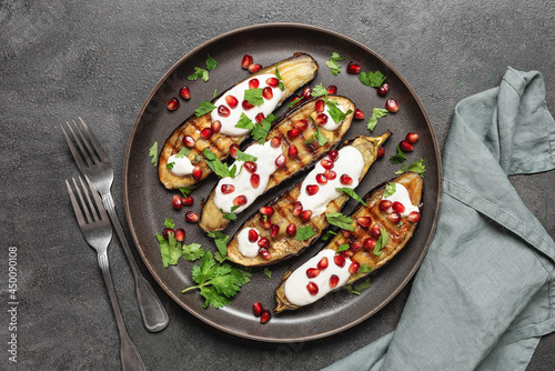 Grilled eggplants with pomegranate, yoghurt garlic sauce and cilantro on a black stone background. Top view, flat lay. Healthy Mediterranean cuisine, vegetarian food.
