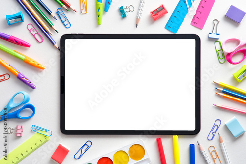 Photographie Digital tablet with blank white screen and frame of colorful school supplies on white background