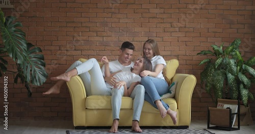 Handsome young man and two beautiful women on sofa at home. Polyamory concept