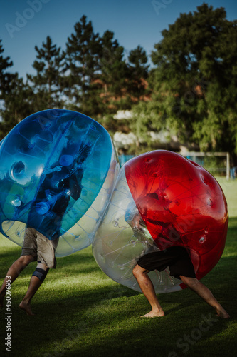 People playing in Bubble Football. Zorbing bumper football soccer on a green field