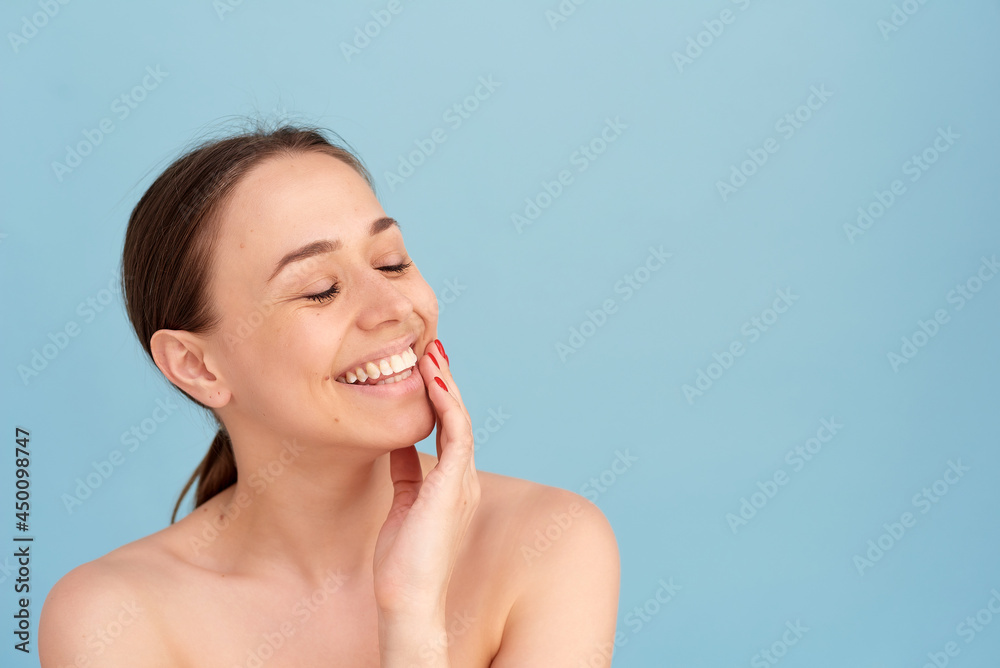 Smiling woman touching her face against a blue background. Natural beauty concept, happy woman Smiling woman touching her face against a blue background. Natural beauty concept, happy woman