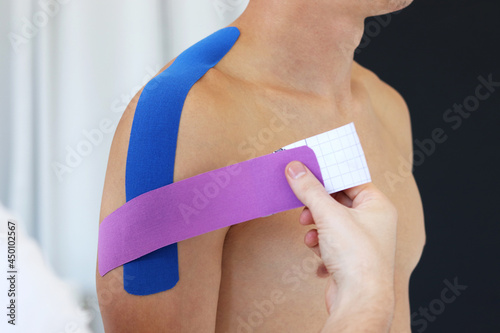 Kinesiology taping. Physical therapist applying kinesiology tape to patient shoulder. Male therapist treating injured shoulder of male athlete. Post traumatic rehabilitation  sport physical therapy.