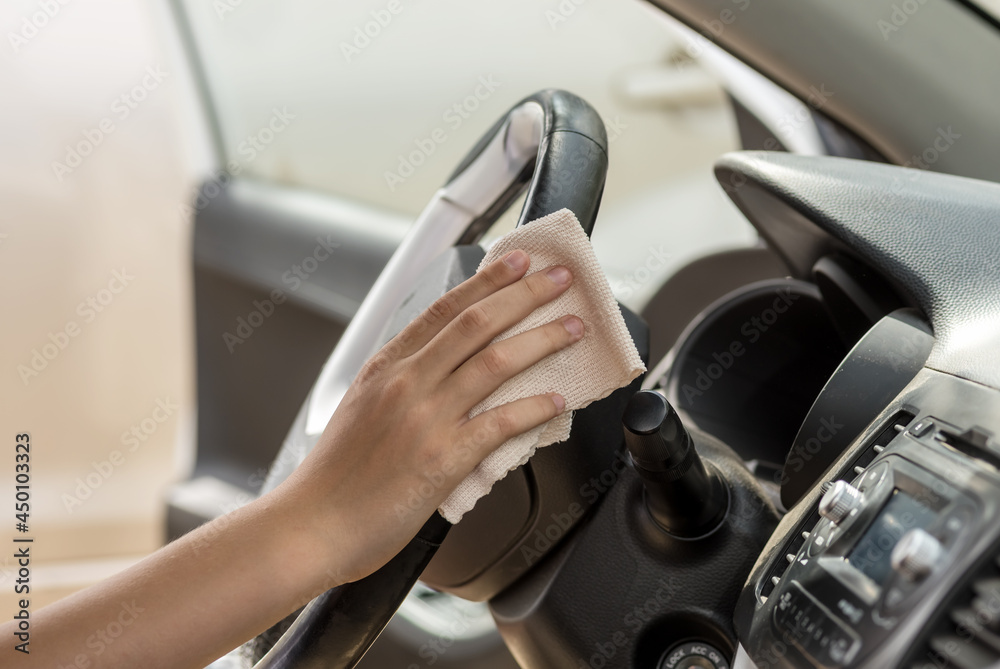 A human hand wipes the steering wheel in a car with a rag. Wipe clean with a cleaner.