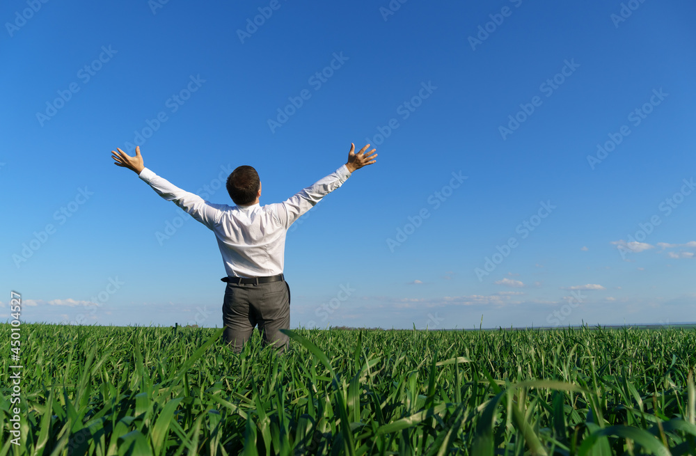 businessman poses in a field, he looks into the distance and rests, green grass and blue sky as background businessman poses in a field, he looks into the distance and rests, green grass and blue sky as background