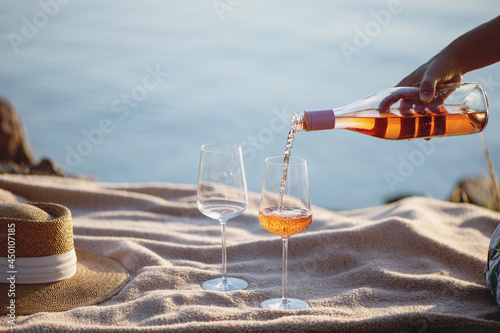 Woman hand pouring rose wine from bottle into glasses on the beach.