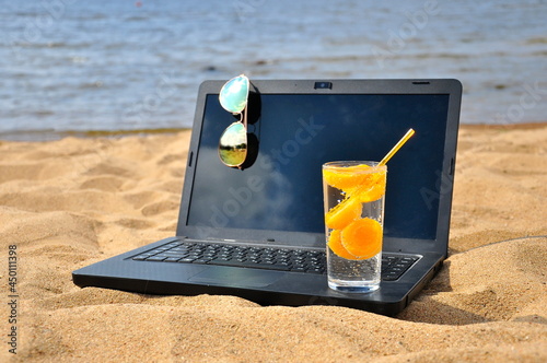 Remote work, a black laptop and sunglasses on a sandy beach.