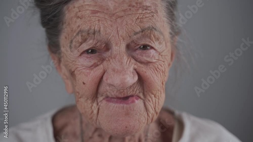 Portrait of Caucasian toothless senior woman 90 years old with deep wrinkles and gray hair cute smiling and talking on gray background in studio. Old female with dental problems. Orthodontist patient. photo