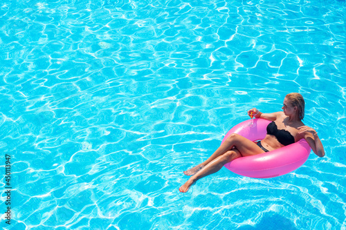 A young woman swims on a pink inflatable circle in clear blue water. A girl with a cocktail relaxes in the pool