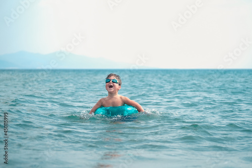Cute smiling boy having fun in the sea and swimming with inflatable ring.