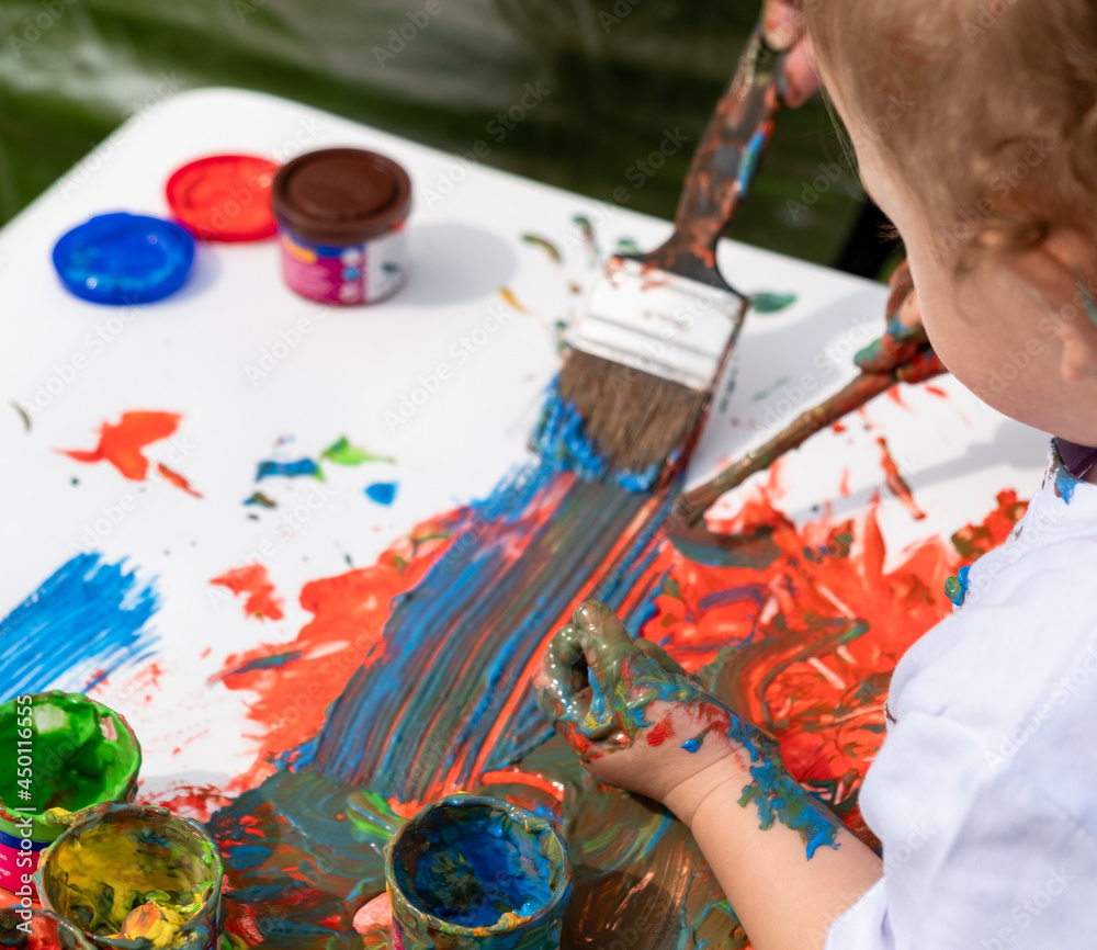 Obraz premium A small child learns to paint with his parents on a white sheet of paint.