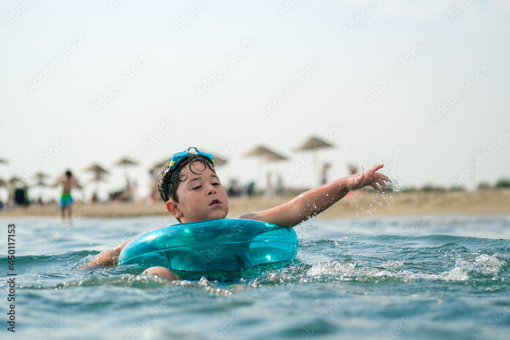 happy boy enjoying swimming in the sea with rubber ring. Learning how to swim