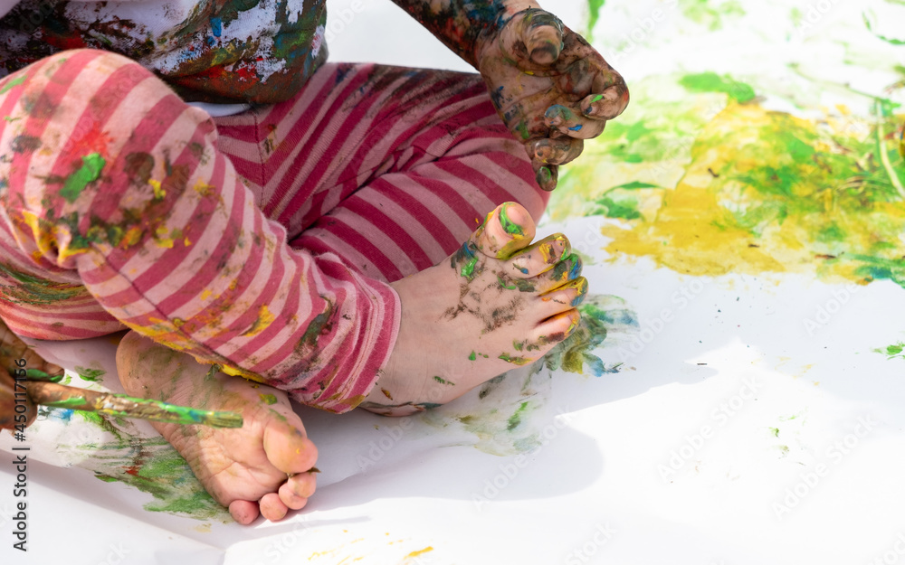 A small child sits in a lotus position and draws with paints on paper.