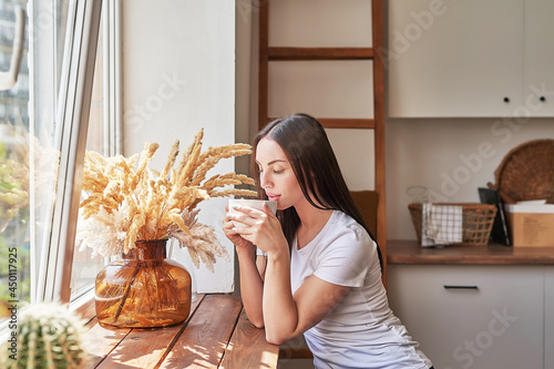 Young woman with cup of coffee or tea at window in coffee shop. Good morning concept. Cozy breakfast. Girl in cafe.