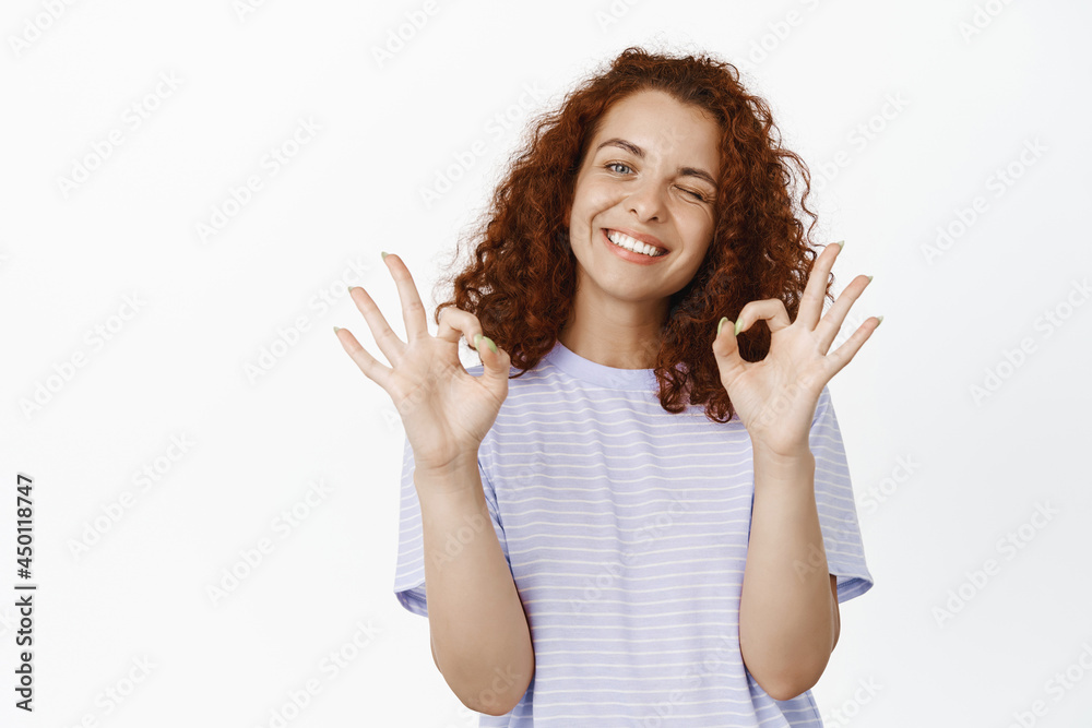 Positive ginger girl winking, smiling and showing ok, okay signs, excellent choice, praising you, like and agree, approve smth good, standing over white background Positive ginger girl winking, smiling and showing ok, okay signs, excellent choice, praising you, like and agree, approve smth good, standing over white background