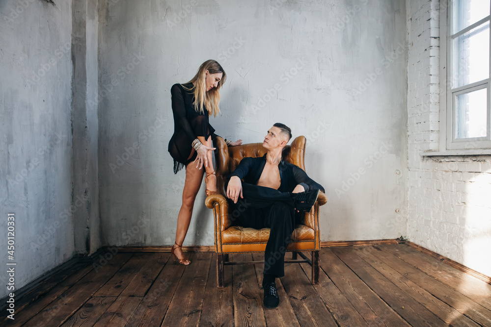 Portrait of Couple two professional ballroom dancers in loft studio on Brown leather sofa. Sport life concept. Passion and emotional dance.