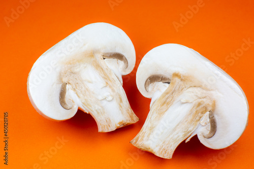 Close up photo of champignon mushrooms on orange background. Mushroom cut in half, inside, macro view.