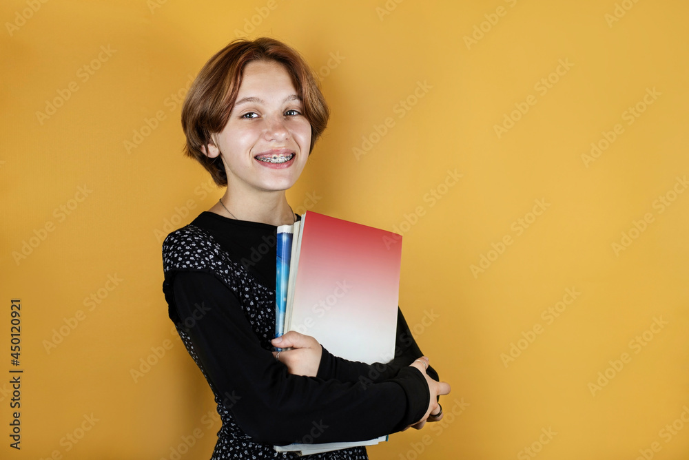 On a yellow background, a young girl with books and notebooks in her hands going to school, a girl smiling, happy to return to school. The girl loves to study On a yellow background, a young girl with books and notebooks in her hands going to school, a girl smiling, happy to return to school. The girl loves to study