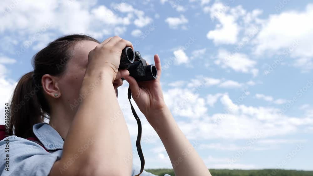 Happy woman with a tourist backpack looking through binoculars at a beautiful landscape.