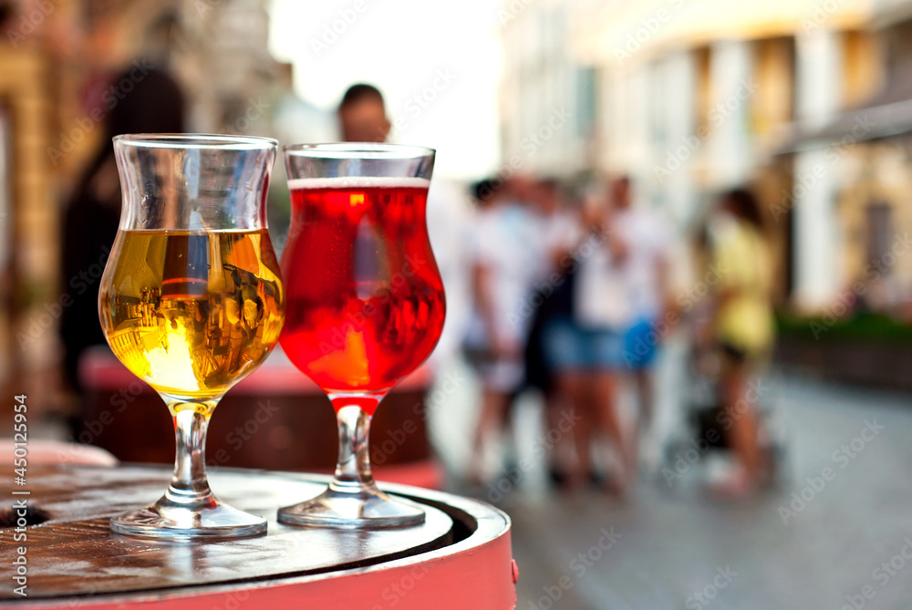 Glass of red and white wine close up. Alcoholic liqueur on a wooden barrel on a background of the city. Blurred people in the background.