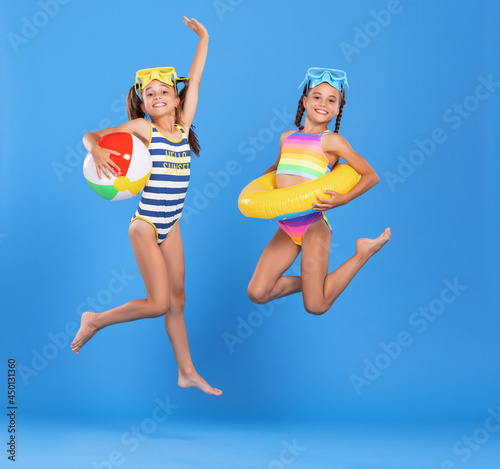 Two funny little sisters in swimsuits and goggles jumping up in air with inflatable swimming ring and ball © JenkoAtaman