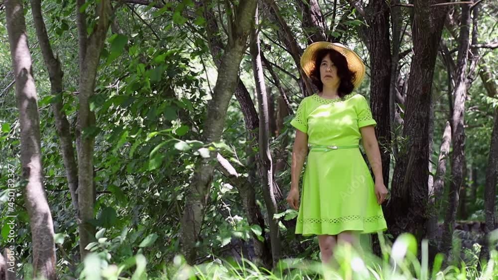 A girl in a straw hat comes up to a tree and plucks some leaves A girl in a straw hat comes up to a tree and plucks some leaves