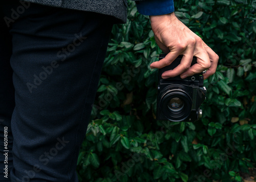 Male hand holding a vintage film camera in the air. Green nature in the background.