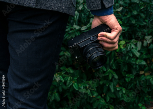 Male hand holding a vintage film camera in the air. Green nature in the background.