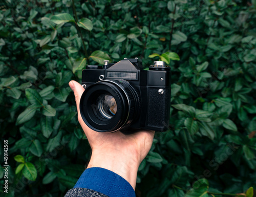 Male hand holding a vintage film camera in the air. Green nature in the background.