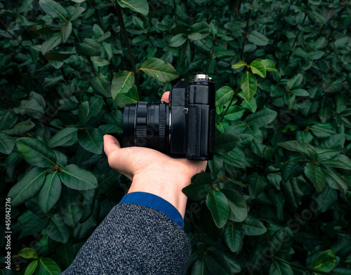 Male hand holding a vintage film camera in the air. Green nature in the background.