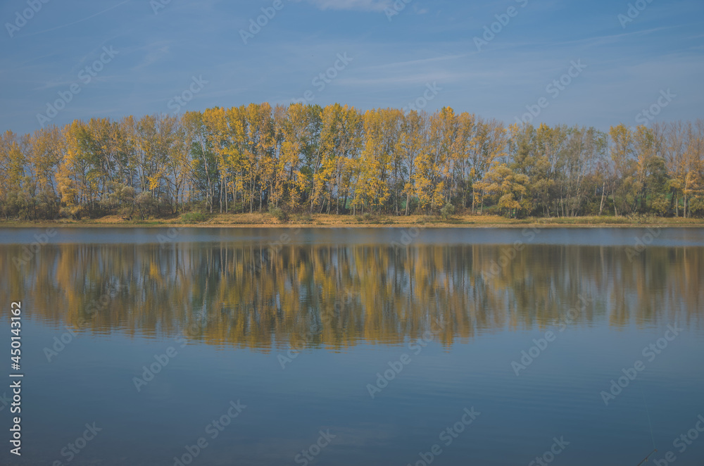 colors of autumn, yellow trees and blue pond in scenic countryside