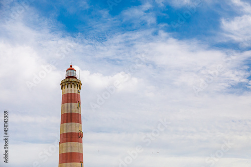 View of the beach and the lighthouse of Praia da Barra on a summer day against a blue sky.