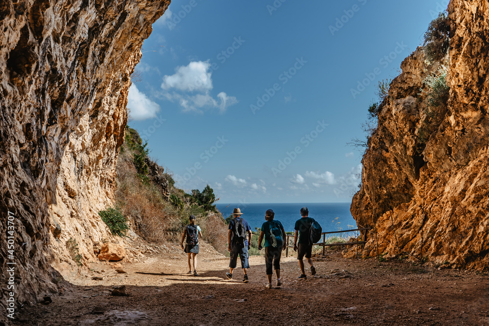 Silhouettes of family on active holiday back view.Group of two seniors and two adults trekking in rocky mountains,Sicily,Italy.Happy multi-generation family walking along coast.Enjoying time together