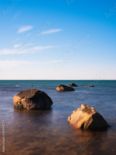 Five glacial rocks in the shallow seawater. Zen-like seascape with old stones and white clouds in the blue sky.