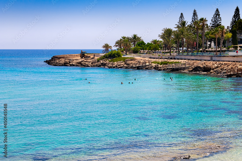 View of the Mediterranean Sea with clear water. The rocky coast of the resort village of Protaras on the island of Cyprus. Swimming people in the distance.