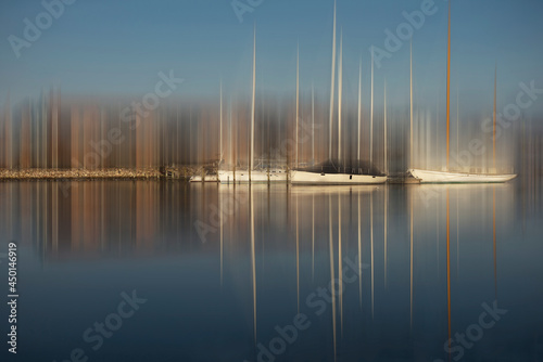 Dreamy blurred photo art of sailboats with masts in a harbor with brown buildings