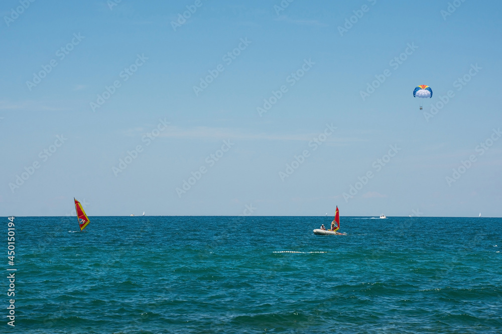 People windsurfing off the Adriatic Sea coastline in July north of Novigrad, Istria, Croatia. A parascender, or parasailer, is in the background
