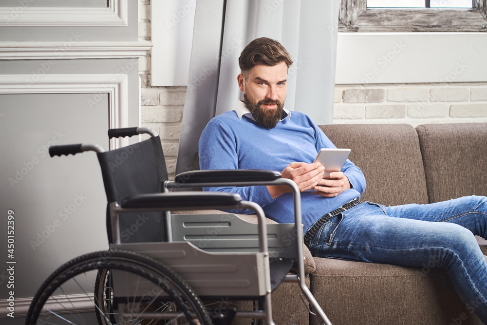 Portrait of a man with disability laying on a couch and using a tablet computer Portrait of a man with disability laying on a couch and using a tablet computer