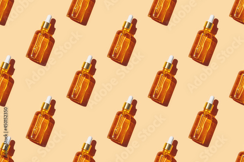 Seamless pattern of anti aging serum in glass bottle with dropper on pastel orange background. Creative layout, cosmetic seamless pattern, flat lay. For packaging design, printing on fabric, paper