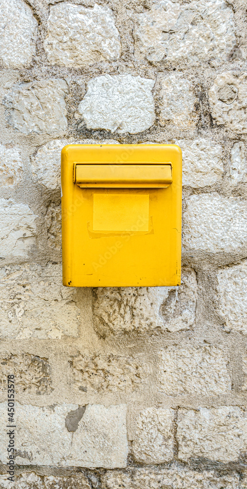 A yellow mailbox on a light stone wall. Box for letters and postcards.