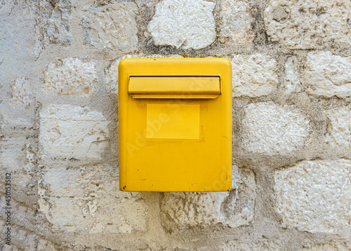 A yellow mailbox on a light stone wall. Box for letters and postcards.