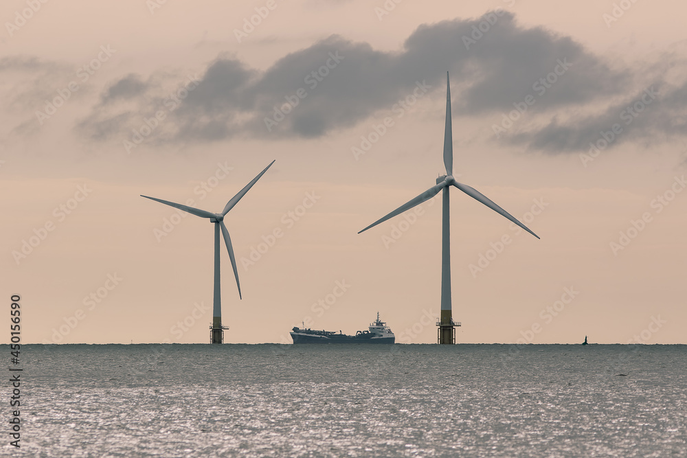 Pair of offshore wind farm wind turbines with supply ship. Clean energy production industry.