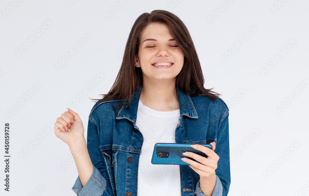 Happy satisfied girl in casual wear holding mobile phone, isolated over blue background Happy satisfied girl in casual wear holding mobile phone, isolated over blue background