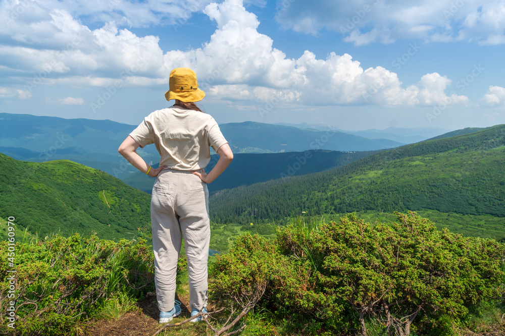 Traveler in hat and backpack resting in nature. A tourist girl looks at the panorama of the mountains. Mountain beautiful landscape Traveler in hat and backpack resting in nature. A tourist girl looks at the panorama of the mountains. Mountain beautiful landscape