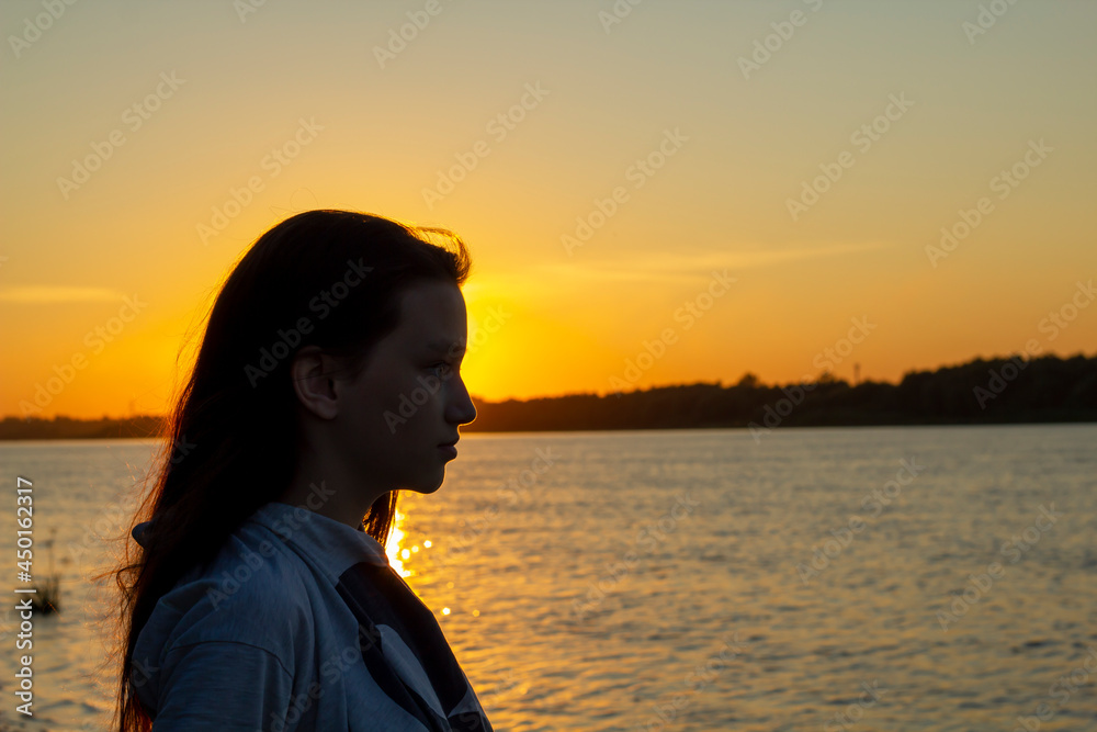 Silhouette of the young girl on a background of the sunset at coast of the river.