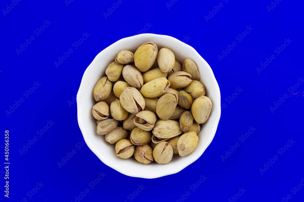 Pistachios in a white plate on blue background Pistachios in a white plate on blue background