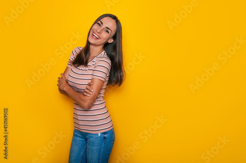 Happy confident beautiful young brunette woman in a t-shirt is posing and having fun isolated on the yellow background