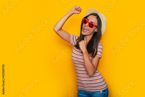 Happy excited beautiful tourist woman in hat and sunglasses is posing on yellow background and having fun